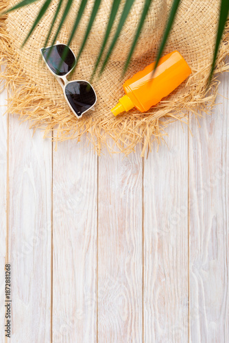 Vacation travel planning simple background of straw hat sunglasses palm leaves and sunblock lotion on white planks flat lay with copy-space