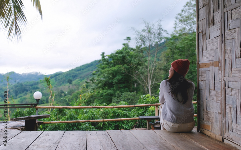 Fototapeta premium A woman sitting on wooden balcony, looking at mountain views on cloudy morning