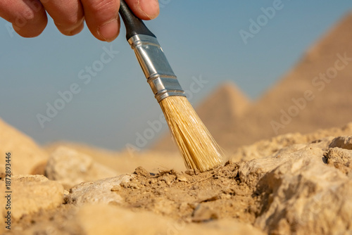 Hand holding a brush to clean dirt from rocks at an archaeological site in the desert during daylight