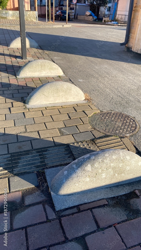 Obraz premium Rounded concrete bollards are aligned along a paved walkway, serving as barriers to prevent vehicle access on sidewalks.