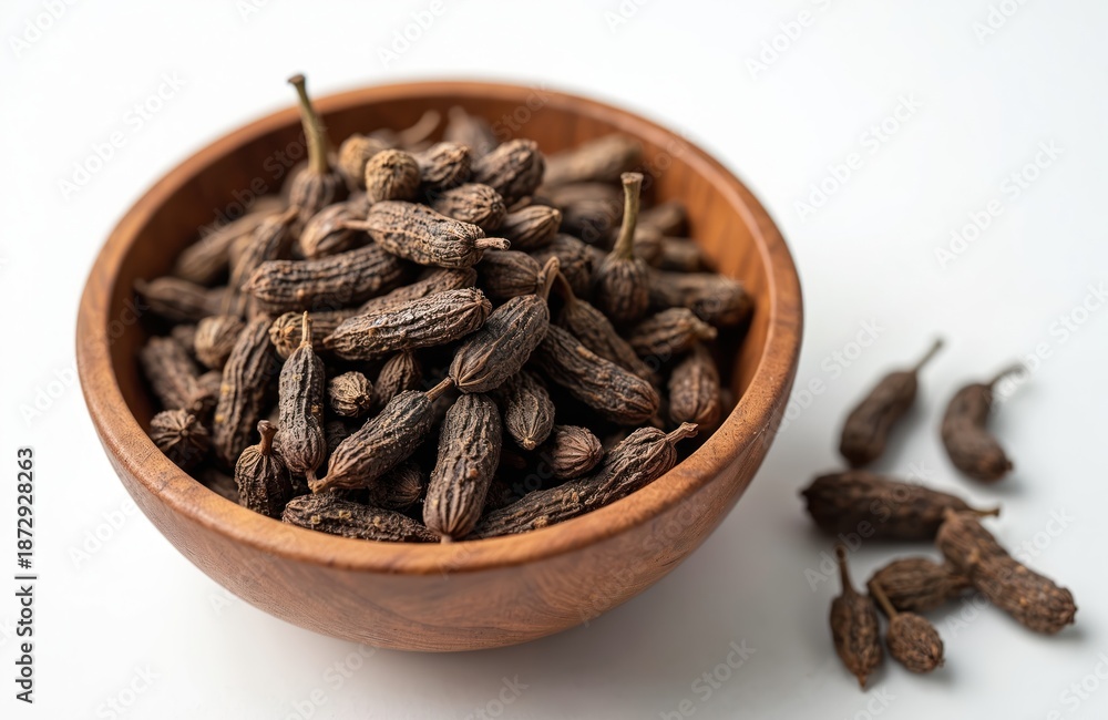Fototapeta premium Wooden bowl full of dried Indian long pepper. Piper longum spice on white background. Hot aromatic seasoning in heap for flavouring tasty meals, cooking.