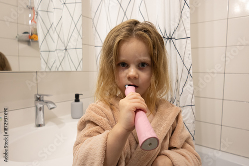 Cute little girl in brushing her teeth with electric toothbrush in bathroom
