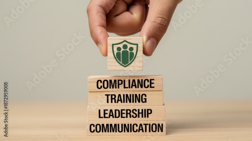 A hand carefully places a block with a shield symbol onto a stack representing compliance training leadership and communication