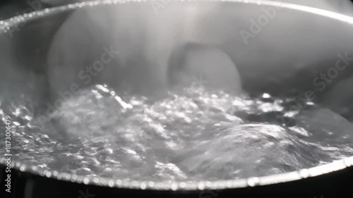 Close up of boiling water in a metal pot with rising steam