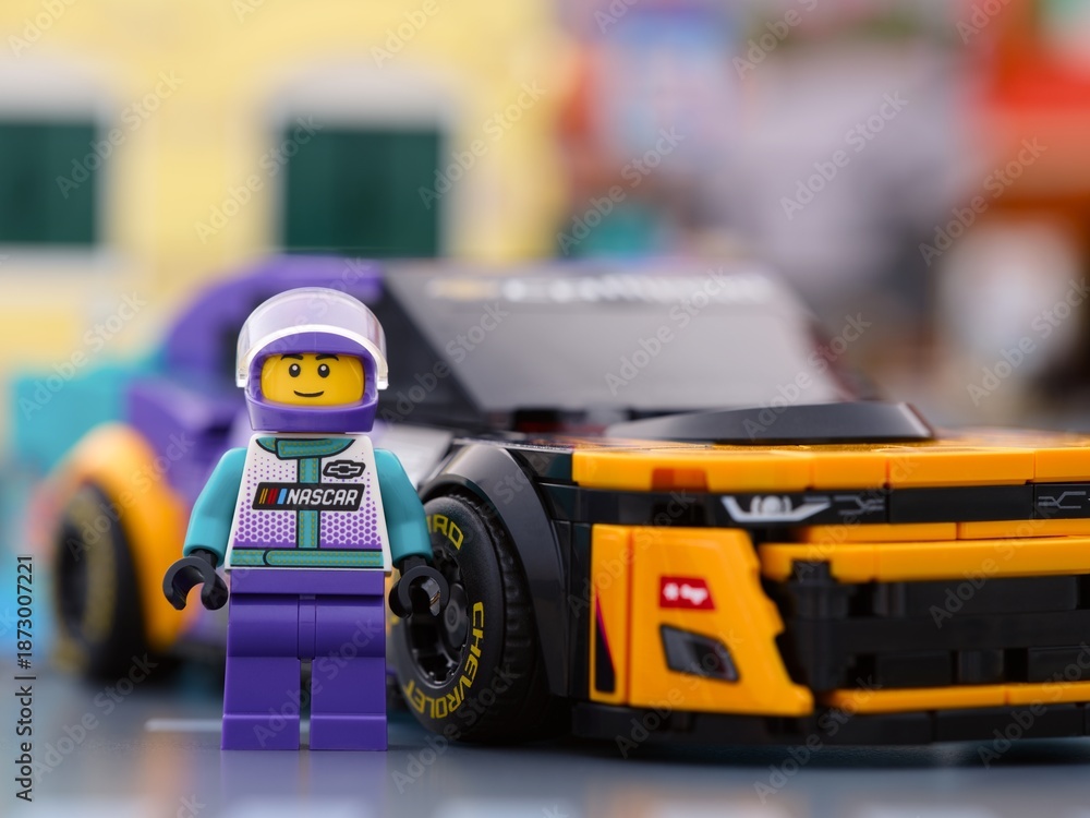 Fototapeta premium Tambov, Russian Federation - January 02, 2026 Lego NASCAR Next Gen Chevrolet Camaro ZL1 driver minifigure standing near his car in city street. LEGO Speed Champions.