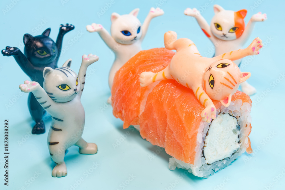 Fototapeta premium Funny plastic toy kittens dancing around delicious salmon sushi rolls. One cat is lying on top of the food. Concept of joy and sushi ordering on blue background. Photo