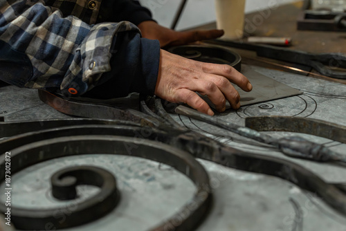 Photos Gros plan sur les mains d’un artisan ferronnier en atelier travaillant des pièces métalliques décoratives, illustrant la fabrication sur mesure et le savoir-faire traditionnel