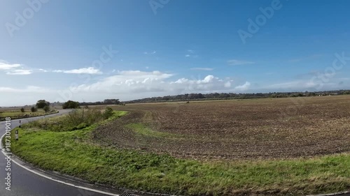 Asphalt road curve passing by plowed agricultural field under blue sky