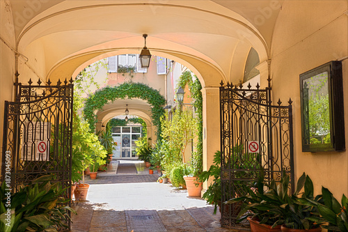 Through an archway leading to a courtyard in Rimini. Potted plants line the path, adding greenery to the setting. The area is quiet and inviting for exploration. Rimini, Emilia-Romagna, Italy
