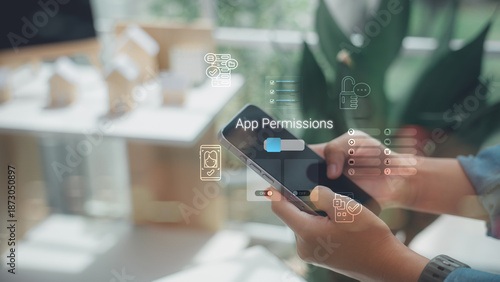 A person using a smartphone to manage app permissions and privacy settings with digital interface icons, focusing on data security and mobile protection in a home office setting.
