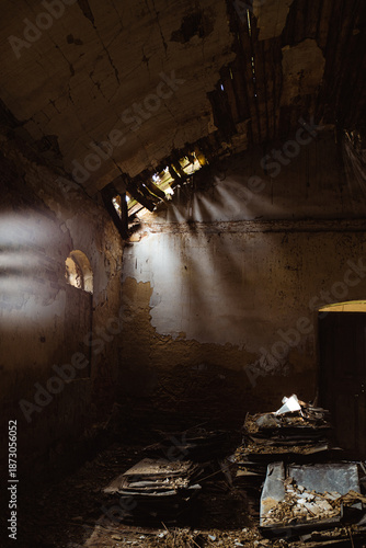 Light shines through a broken roof in an abandoned building, revealing dust and debris on the floor at a forgotten location