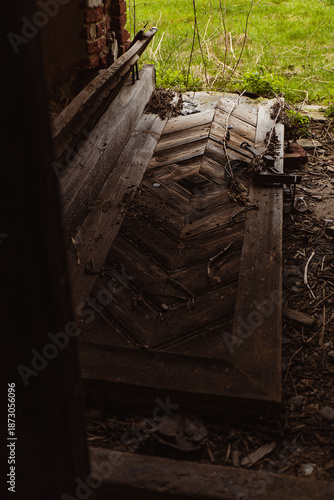 Old wooden door lies on the ground inside a building with grass visible outside in daylight