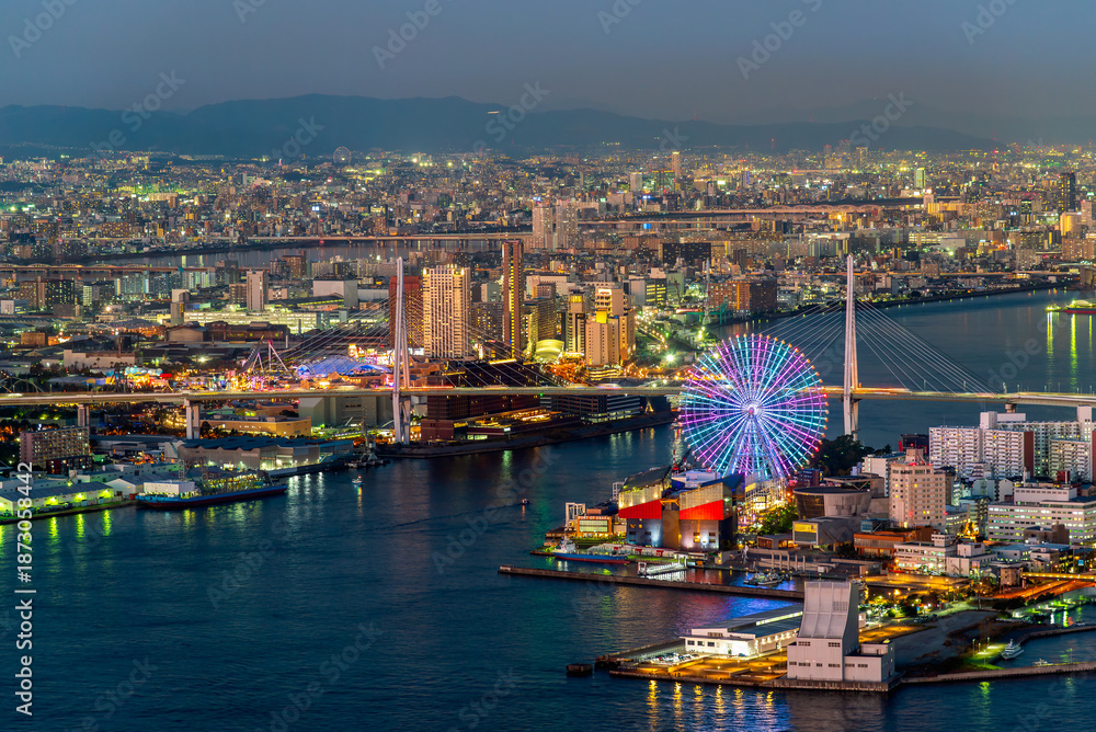 Fototapeta premium High angle night view of Osaka Bay with illuminated Tempozan Ferris Wheel and Minato Bridge. Vibrant cityscape of Osaka, Japan, at twilight with glowing urban lights and beautiful harbor skyline.