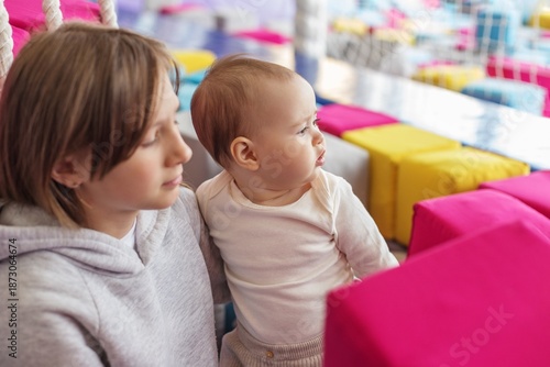 Tablou pe pânză Older sister holding baby at indoor playground. Family time