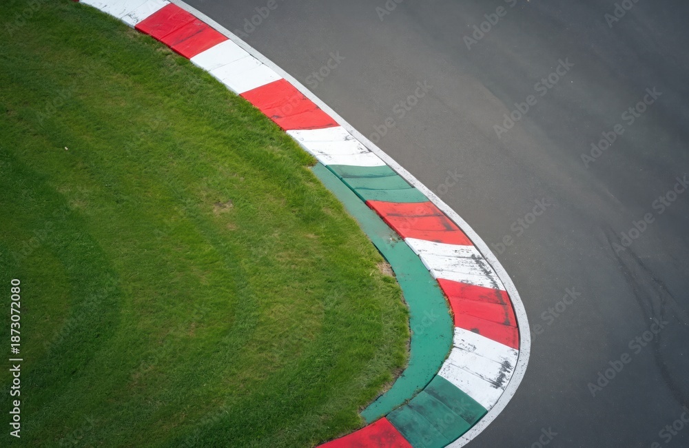 Fototapeta premium Aerial photo of race track corner. Red and white curb marks edge. Green grass separates asphalt and safety feature. Motorsports, speed theme.