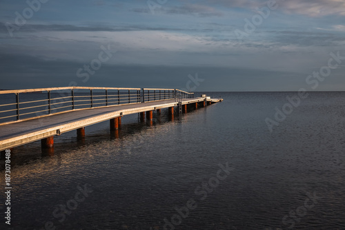 A quiet wooden pier stretching into calm sea water under a dramatic cloudy sky, creating a peaceful and minimal coastal scene.