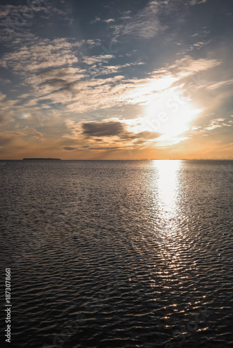 A golden sunset reflecting across calm sea water under a dramatic sky, creating a peaceful and atmospheric seascape.