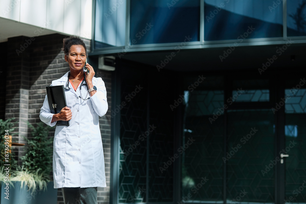 © Lumos sp - Portrait of a female woman doctor or nurse and health care worker using a smartphone mobile phone in front of hospital or clinic outside © Lumos sp - Portrait of a female woman doctor or nurse and health care worker using a smartphone mobile phone in front of hospital or clinic outside