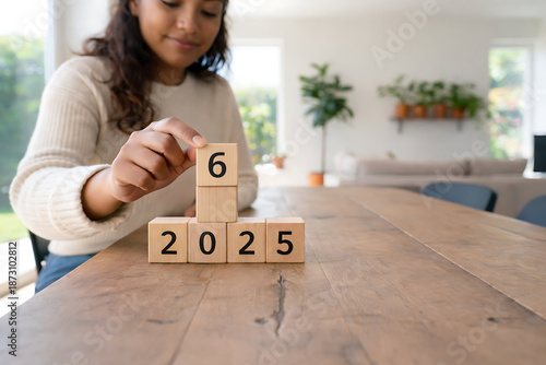 Visualizing Future Goals: A focused individual meticulously places the number '6' atop wooden blocks displaying '2025', symbolizing the setting and pursuit of personal or professional objectives.