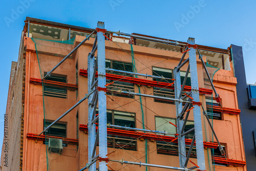 Obraz na płótnie Building Facade Reinforced with External Steel Structure, Urban building exterior under renovation, featuring external steel framework and scaffolding for structural reinforcement