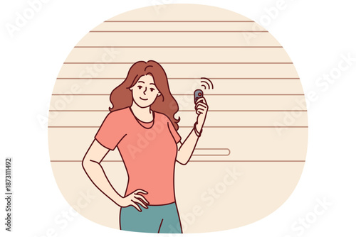 Woman stands near garage door pvc and uses electronic key to automatically open or close entrance. Girl driver poses at garage to securely store own car and protect personal vehicles from theft