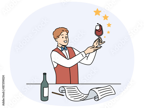 Man sommelier holds glass red wine and evaluates taste of noble alcoholic drink standing near table with bottle and sheet of paper. Guy studying at sommelier school wanting to get job in restaurant