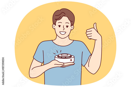 Man with smoke detector gives thumbs up recommending purchase of fire safety equipment. Young guy demonstrating quality smoke detector giving positive feedback after testing gadget
