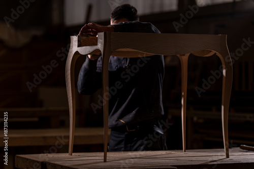 Canvastavla Artisan ébéniste en atelier travaillant sur une table en bois aux lignes élégantes, illustrant la fabrication artisanale et le design de mobilier sur mesure