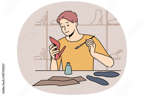 Man shoemaker holding women shoes sitting at table, repairing or making handmade footwear. Professional male shoemaker makes wardrobe items from genuine leather, located in workshop