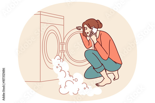 Woman near broken washing machine calls home electronics repairman because of foam pouring out of drum. Excited housewife sitting looking at washing machine with factory defect causing leak