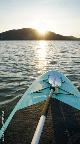 Blue turquoise SUP board in wavy open water. Stand Up Paddle board activity has water sport in the dam during hill in twilight sun. Rowing boat in nature.