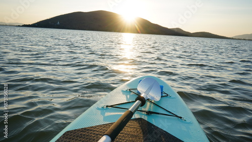 Blue turquoise SUP board in wavy open water. Stand Up Paddle board activity has water sport in the dam during hill in twilight sun. Rowing boat in nature.
