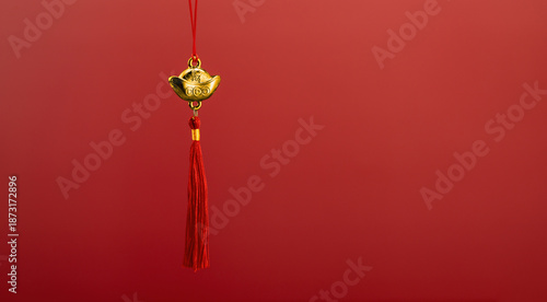 Gold lucky charm with red tassel on red background.