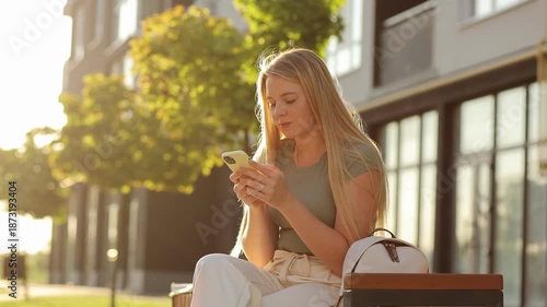 Young woman sending a voice message with smartphone outdoors in an urban park during golden hour