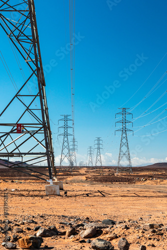 Desert landscape with tall power transmission towers and long lines under bright blue sky