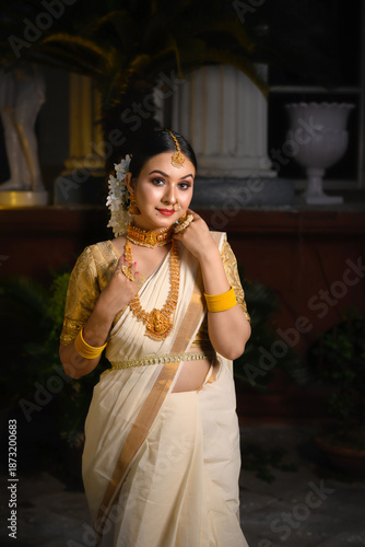 Indian bride wearing a traditional saree and gold jewellery stands before a vintage background