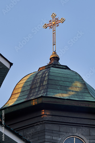 Golden Orthodox cross atop aged church dome against clear blue sky