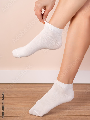minimalist composition focused on a person’s lower legs and feet. The person is wearing clean, white ankle socks made of a soft, stretchy knit fabric. One foot is lifted slightly off the ground while 