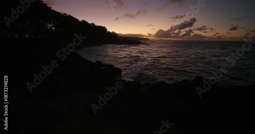 Sunset over the ocean at a rocky shore with silhouettes of trees in the background. Dusk in Dominican Republic.  Jib.
