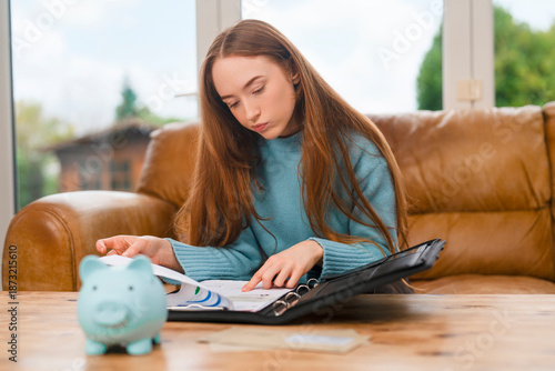 Teen student reviews notes while sitting at home with a piggy bank on the table