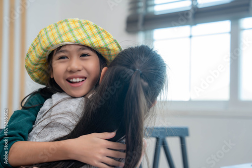 Two young student girls share a warm hug indoors, expressing friendship, happiness, and emotional connection in a bright, cozy classroom environment. Back to school