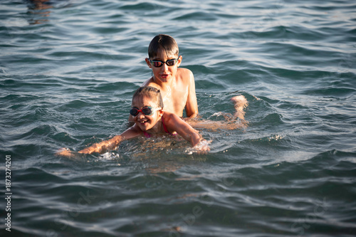 A happy girl is learning to swim. A boy teaches his sister how to swim in the sea.
