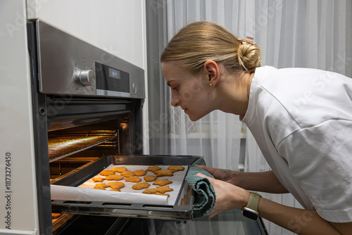 Young mother taking a tray of freshly baked biscuits out of the oven