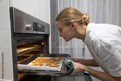 Young mother taking a tray of freshly baked biscuits out of the oven