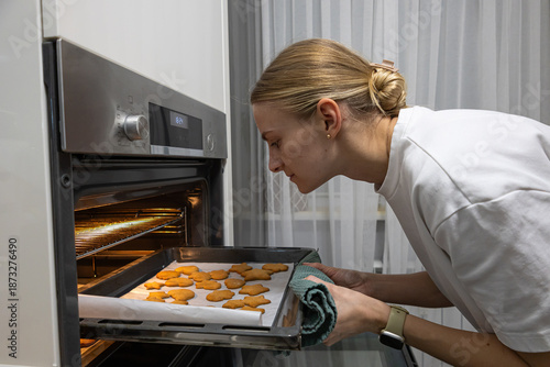 Young mother taking a tray of freshly baked biscuits out of the oven