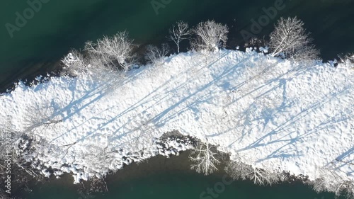 Small island under snow in Mreznica River in Croatia, idyllic rural winter landscape, drone overhead view