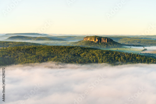 Beautiful summer landscape of Saxon Switzerland National Park in Germany. Isolated Pfaffenstein mountain rising above dense fog. Scenic nature travel and outdoor concept.