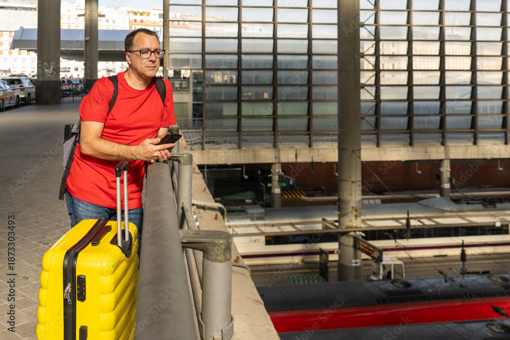 Fototapeta premium Man with yellow suitcase overlooking trains at railway station