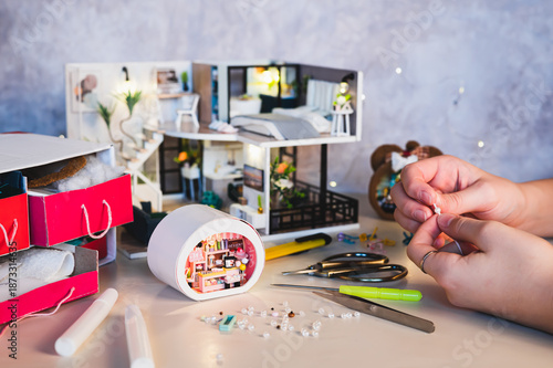 Children's hands string a bead to decorate a tiny house on a table