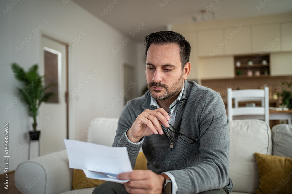 Fototapeta premium Man evaluating finances at home reading letter feeling stressed